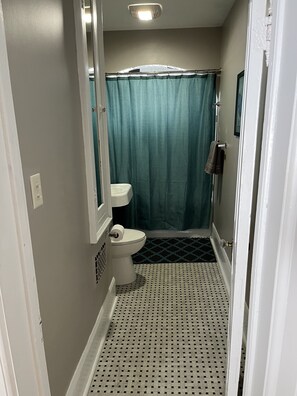 Un baño estrecho con inodoro, cortina de ducha y suelo estampado.