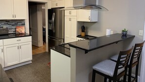 A modern kitchen with white cabinets, a stainless steel refrigerator, a built-in oven, and a bar area with two stools. - Close to Downtown & UWEC (Eau Claire)