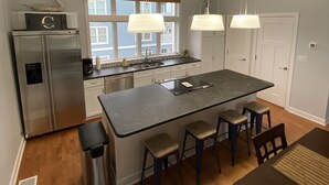 A modern kitchen with a central island, stainless steel appliances, pendant lighting, and a view of the outside through large windows. - Modern 2 Bedrooms, 2.5 Baths in Beautiful IBIS section of Seapointe Village (Wildwood Crest)