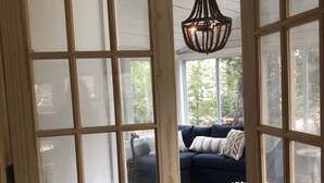 Una porta in legno aperta che dà su un soggiorno con un divano blu scuro, cuscini decorati e una lampada a sospensione.