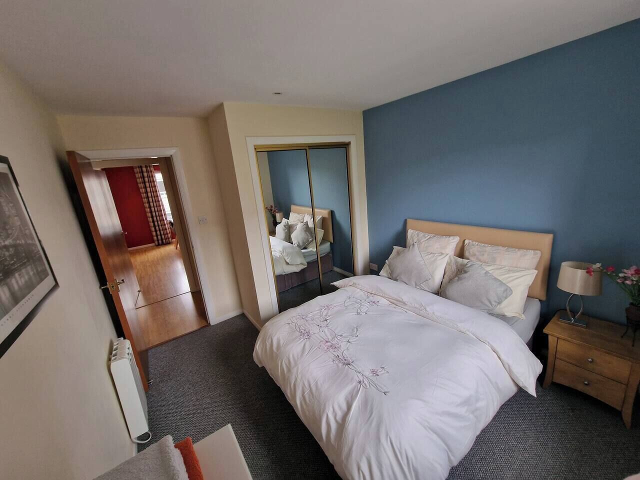 A hotel room with a bed, bedside table, and a mirror.