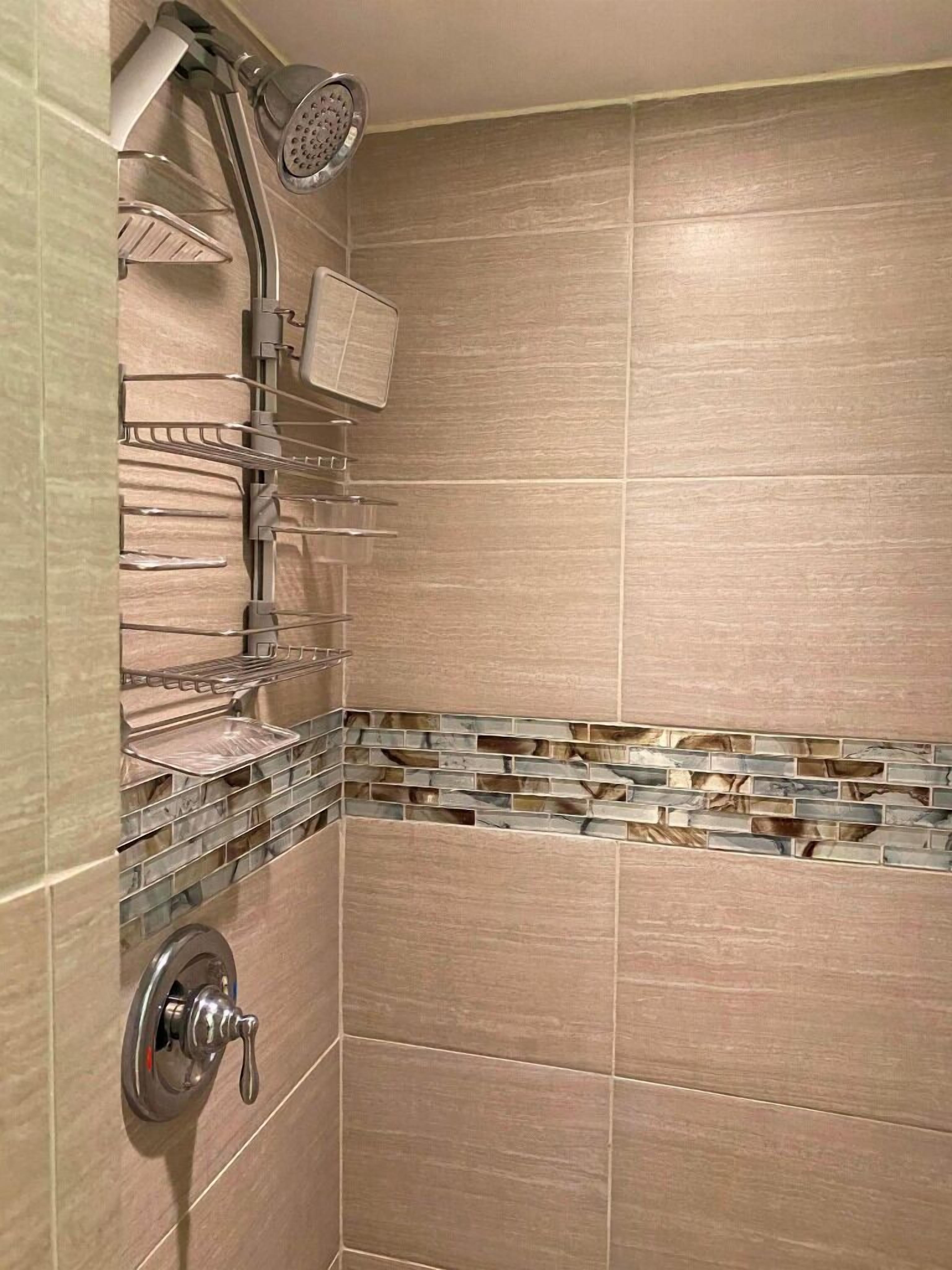 Une douche dotée d’une étagère en verre, d’un pommeau de douche à main et d’un robinet mural.