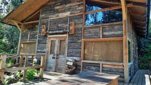 A rustic log cabin with a wooden porch, a central door, and two windows. - Cabañas Rústicas Pucón (Pucon)