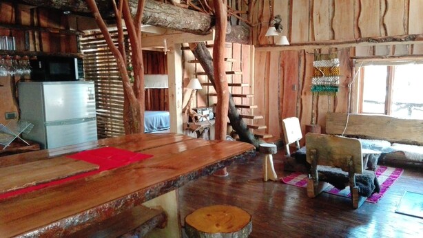 A rustic cabin interior with a wooden dining table, a refrigerator, a radio, and a staircase leading to an upper level. - Cabañas Rústicas Pucón (Pucon)