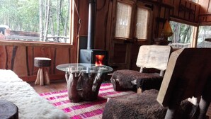 A rustic cabin interior with a glass-top table, wooden furniture, and a visible wood-burning stove. - Cabañas Rústicas Pucón (Pucon)