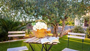 A picnic setup with a wicker basket, a glass of wine, and an open book on a wooden table, surrounded by benches and greenery. - Gorgeous home in Castelvetrano (Castelvetrano)