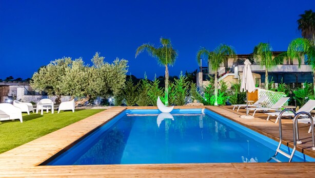 A rectangular swimming pool with a wooden deck, surrounded by palm trees and a well-maintained lawn. - Gorgeous home in Castelvetrano (Castelvetrano)