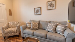 A living room with a grey sofa, patterned armchair, and a coffee table with a remote control. - Top floor upscale contemporary space with great views and great location (Galveston)