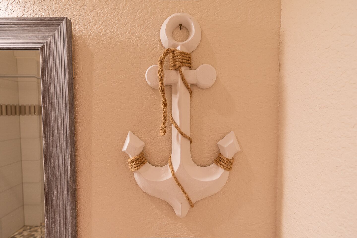 Une décoration en forme d’ancre blanche, ornée d’une corde, sur un mur de couleur beige.