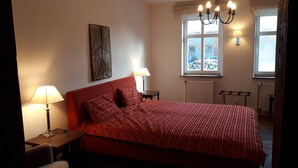 Ein Schlafzimmer mit einem großen Bett, zwei Nachttischlampen, einem Heizkörper, einem Fenster mit Blick auf Felsen und einer Deckenleuchte.