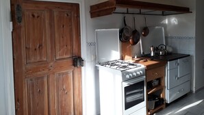 Eine Küche mit Holztür, weißen Geräten und hängenden Töpfen.
