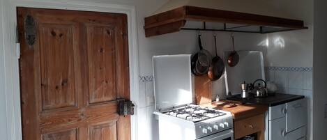 Une cuisine avec une porte en bois, des appareils électroménagers blancs et des casseroles suspendues.