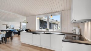 Moderni keittiö, jossa on valkoiset kaapit, suuri ikkuna sekä ruokailutila, jossa on pöytä ja tuolit.