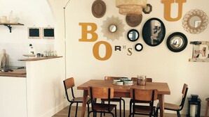 Un comedor con mesa y sillas de madera, una lámpara colgante y adornos en la pared, incluyendo letras y espejos.