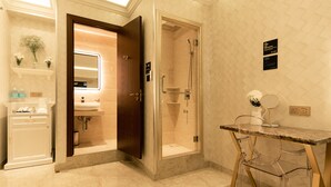 Un baño moderno con ducha, tocador con espejo y una pequeña mesa con un florero.