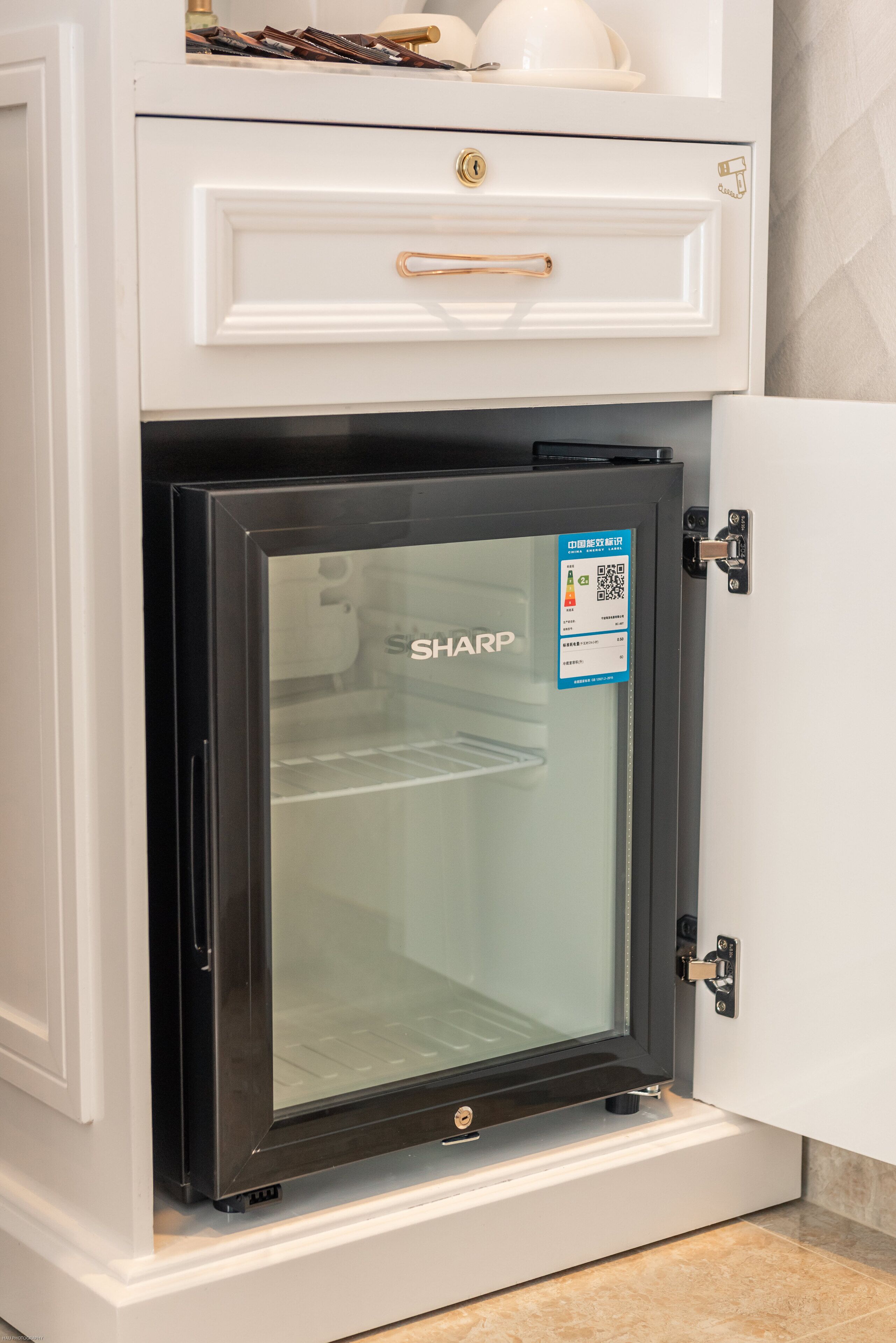 A compact, modern refrigerator with a glass door, a built-in freezer compartment, and a control panel on the door.