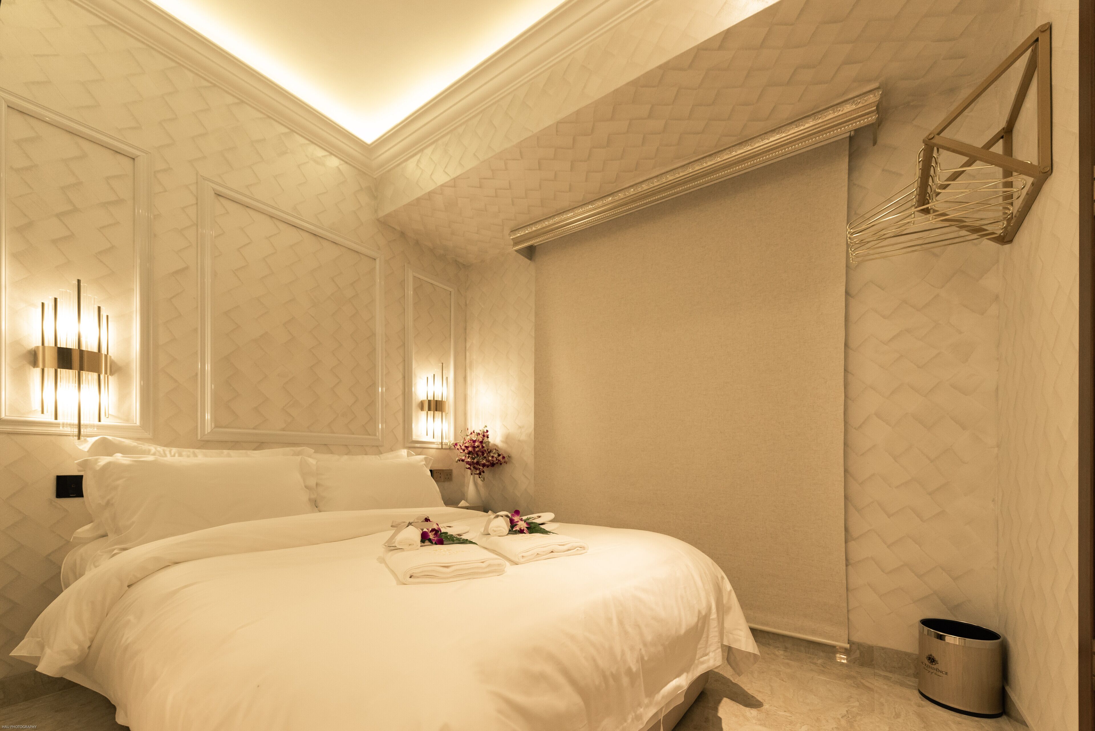 A hotel room with a large bed, a wall-mounted light fixture, and a trash can.