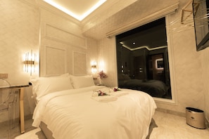 Habitación de hotel moderna con una cama grande, una mesita de noche, un espejo y una ventana con vistas al interior.
