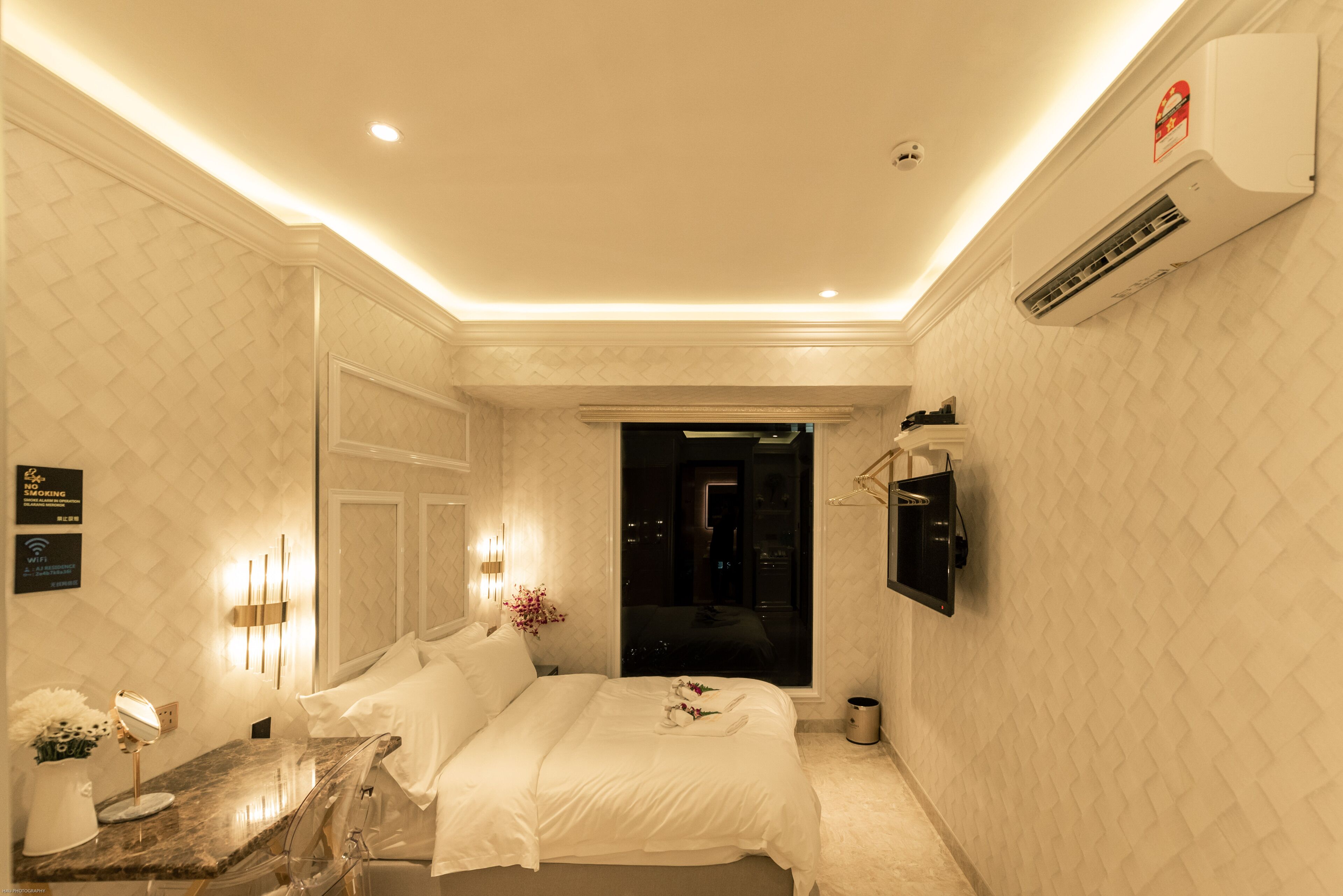 Habitación de hotel con una cama, un tocador con espejo, una mesita con un florero y un equipo de aire acondicionado en la pared.