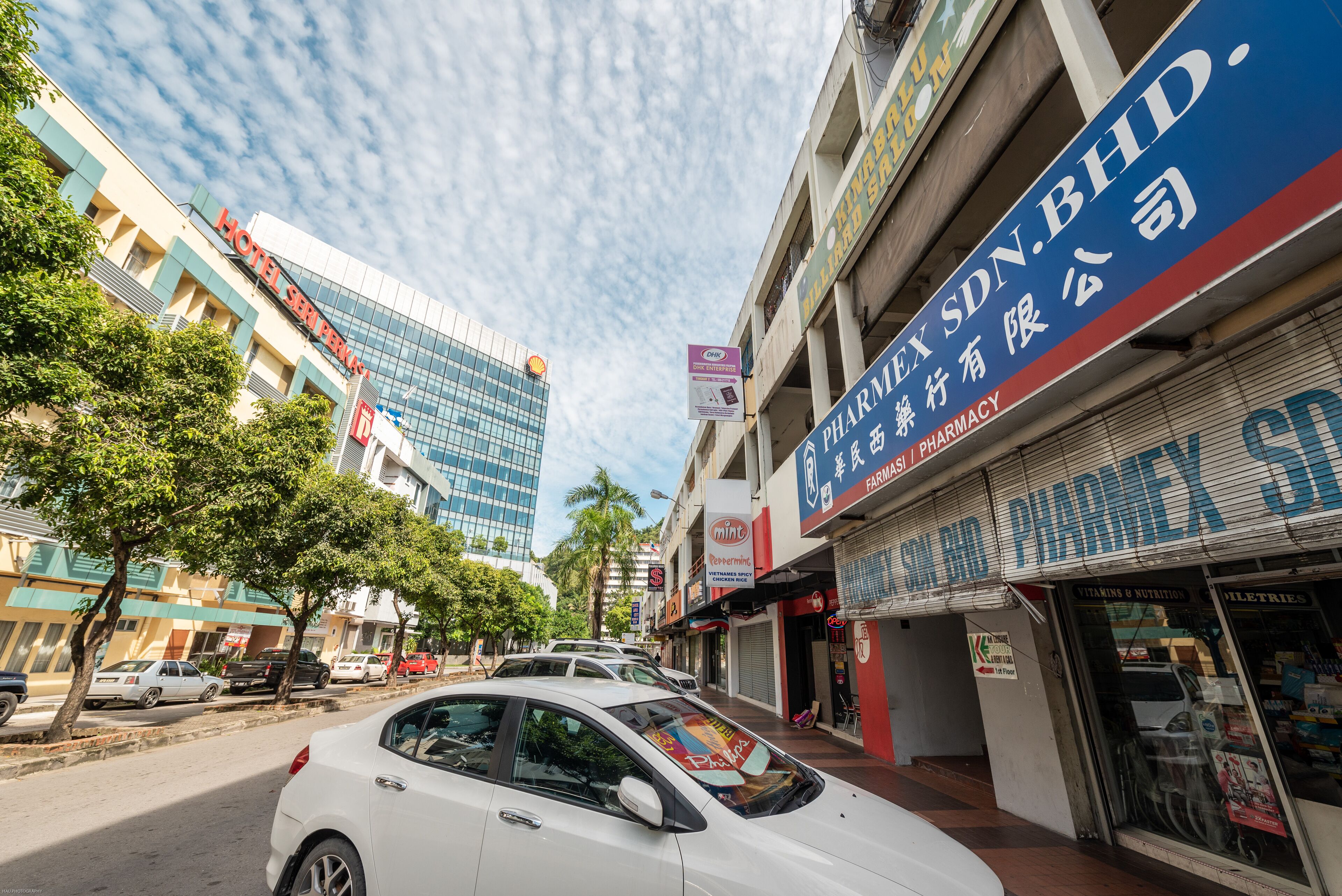 A street view with a pharmacy, a hotel, and a modern building with glass windows.