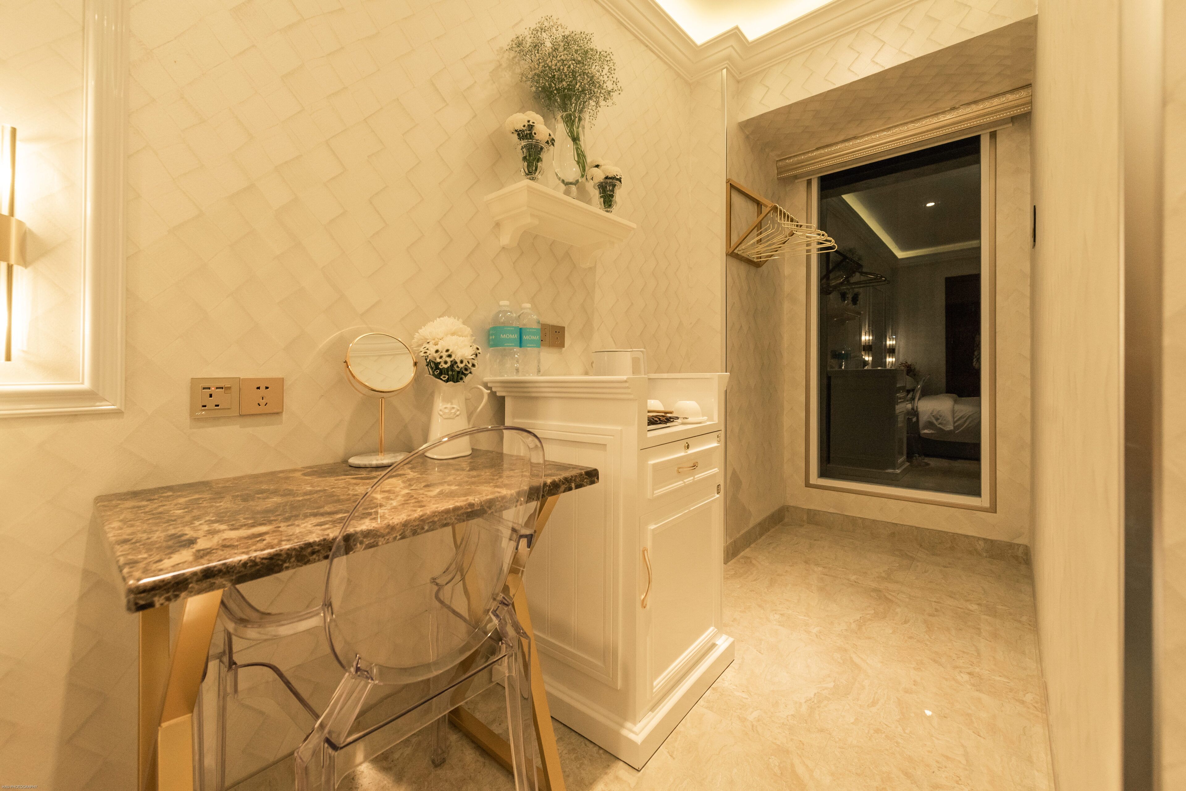Un baño con encimera de mármol, una silla de vidrio, un mueble blanco y una zona de ducha visible a través de un mamparo de cristal.