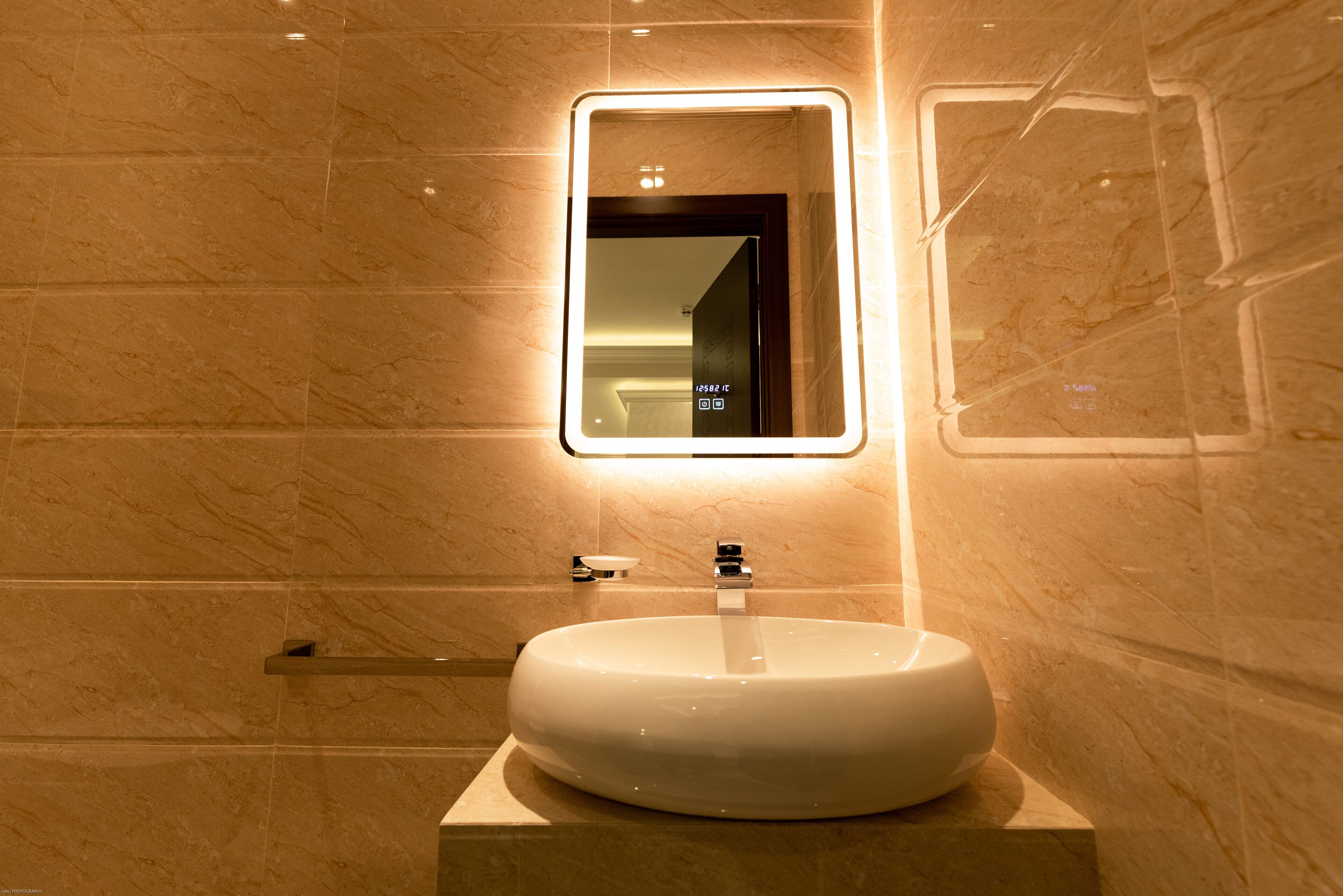 A bathroom with a round sink, a rectangular mirror with a light, and a towel rack.