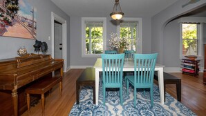A dining area with a wooden piano, teal chairs, a white table, and patterned rugs.