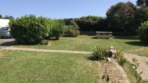A grassy area with a stone pathway, a bench, and dense shrubbery. - Renovated one-bedroom apartment, 300 m from the beach, free private parking (Bénodet)