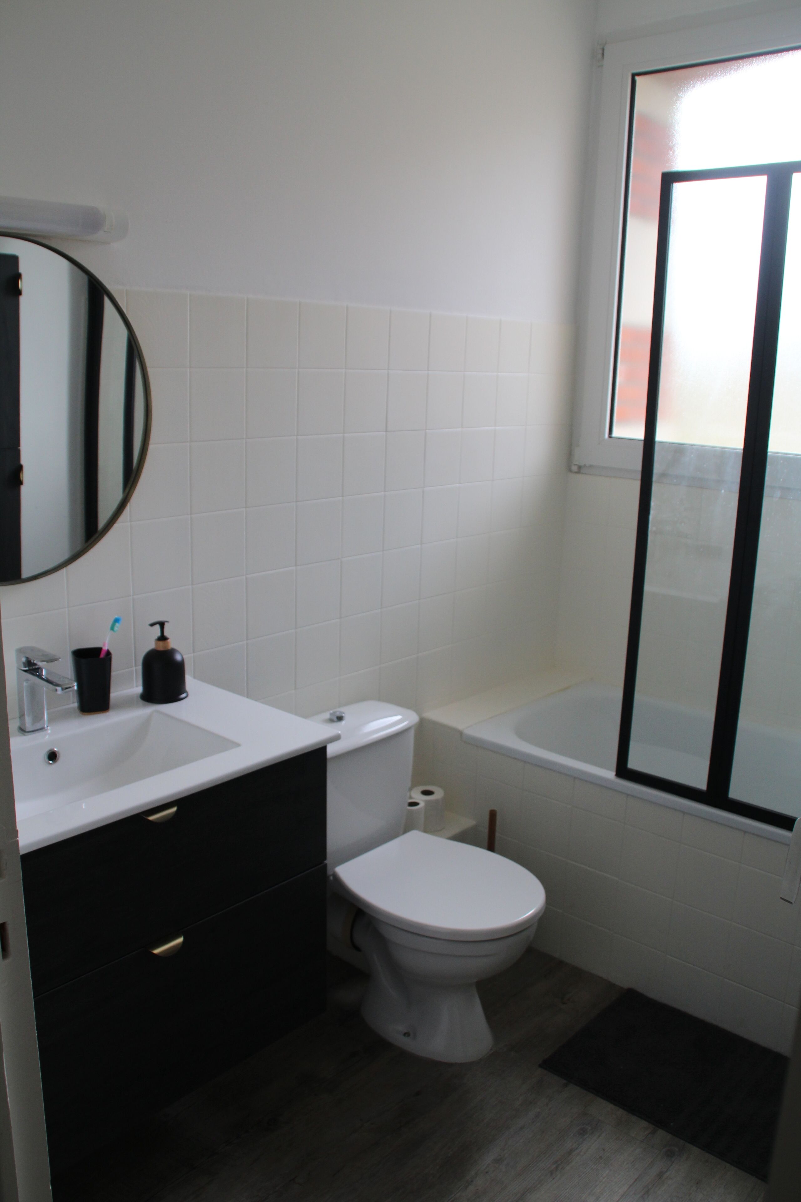 A bathroom with a white sink, black vanity, white toilet, and a bathtub with a glass door.