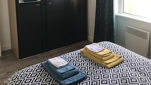 A bedroom with a patterned bedspread, a wardrobe, a mirror, and a window with curtains. - Renovated one-bedroom apartment, 300 m from the beach, free private parking (Bénodet)