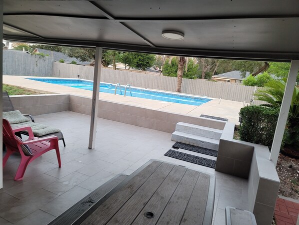 A covered patio with a pool, outdoor furniture, and a view of the backyard.