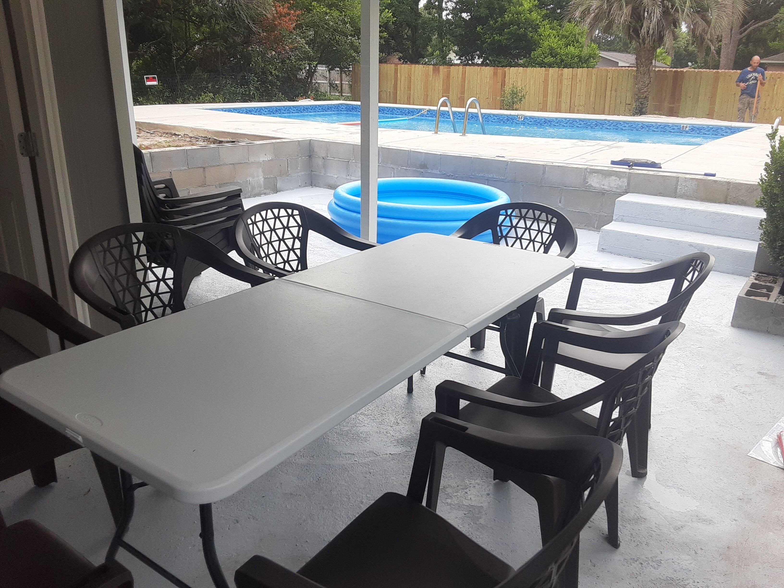 Un patio al aire libre con una mesa y sillas, una piscina y una valla de madera al fondo.