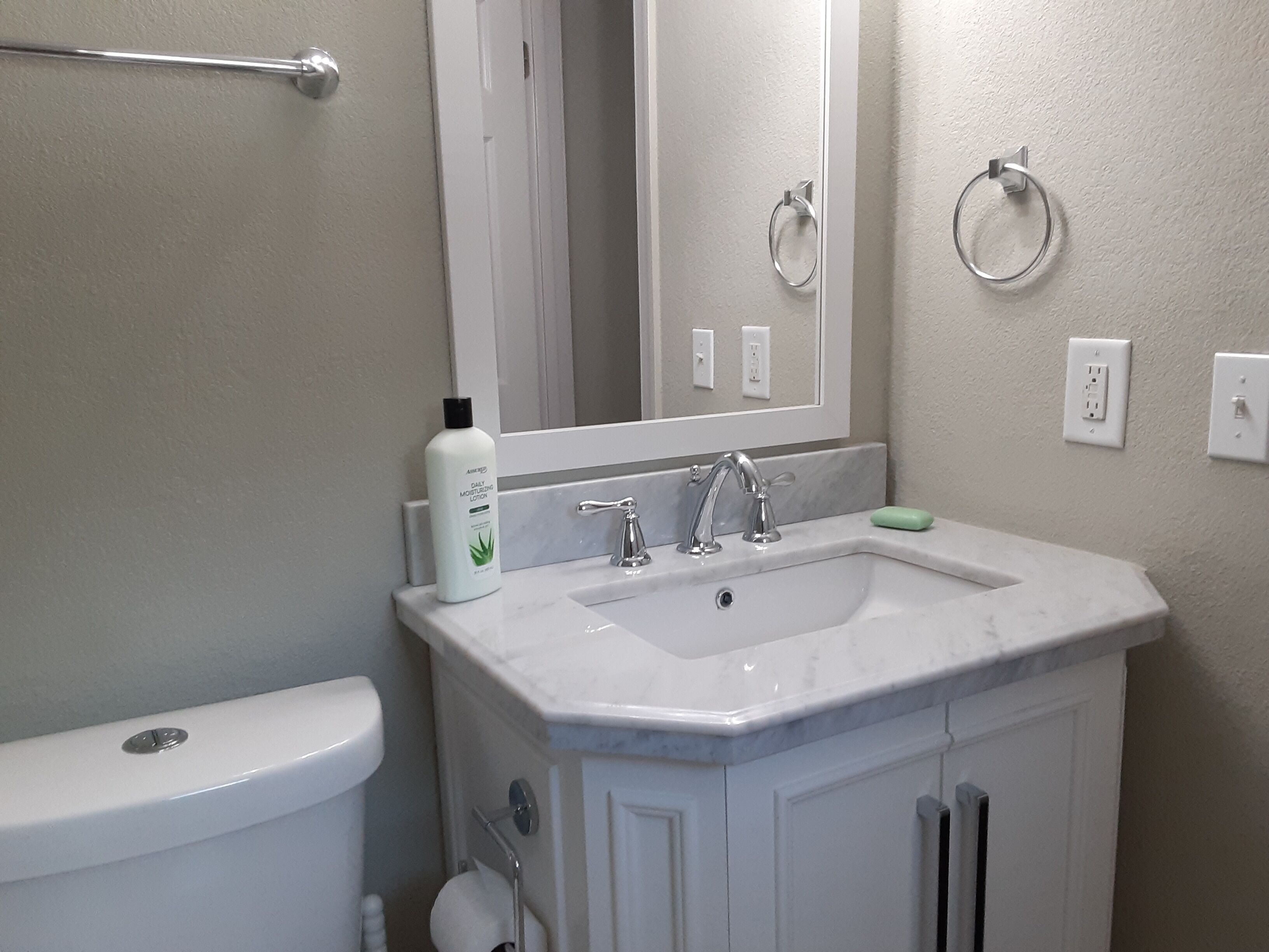A bathroom with a white sink, two faucets, a mirror, a towel ring, and a toilet.