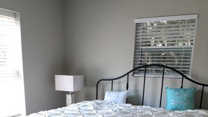 Een slaapkamer met een bed, nachtkastje, lamp en een raam met zonwering.