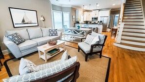 Un salon spacieux comprenant un canapé, des fauteuils, une table basse et un escalier menant à une cuisine.