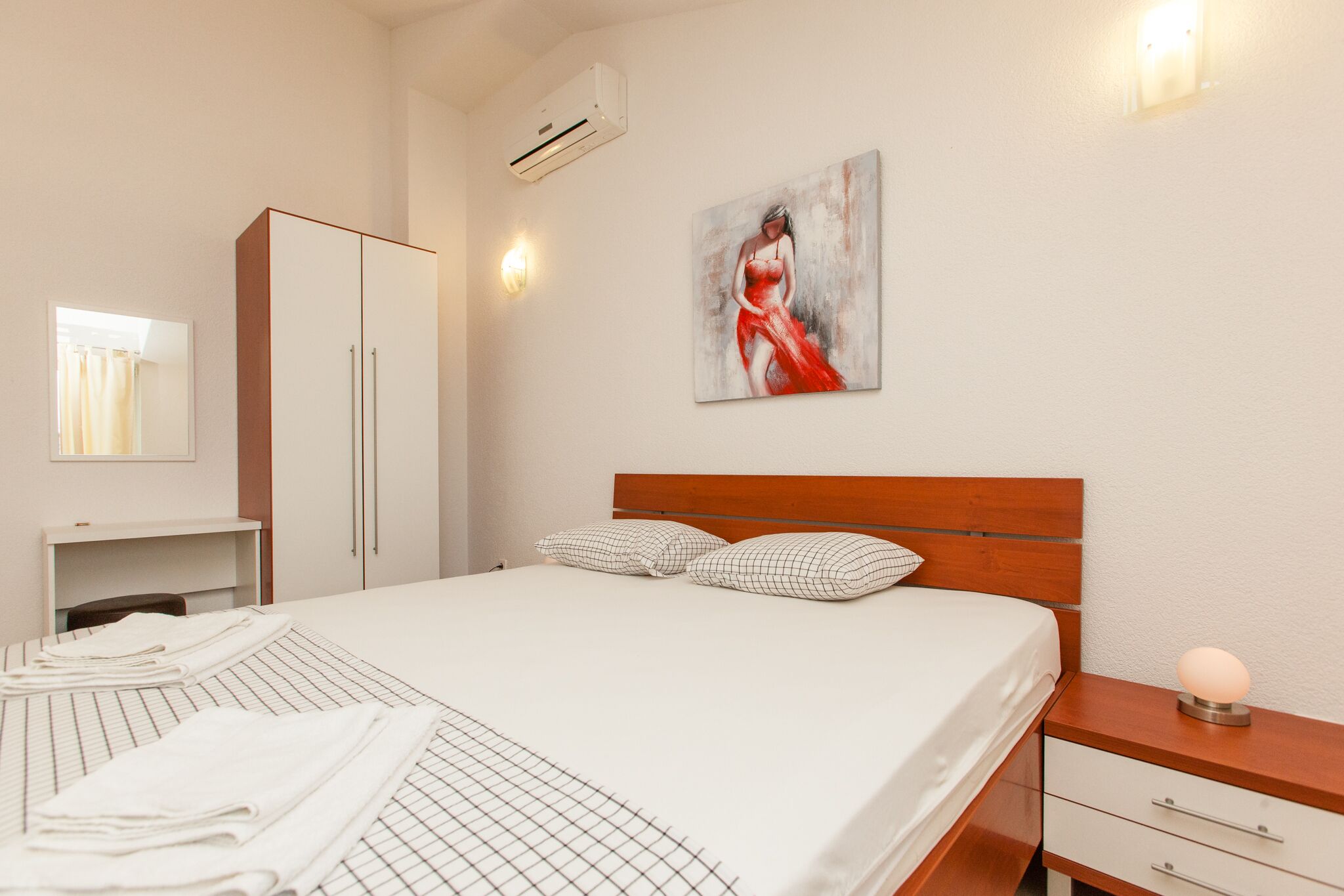 A hotel room with a bed, a wardrobe, a bedside table with a lamp, and a painting on the wall.