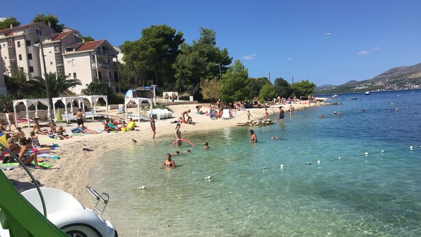 En strand med klart vand, folk der svømmer og strandparasoller.