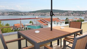 En balkon med et træbord og stole, en rød parasol og udsigt over by og vand.