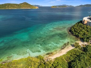 Vista costeira com praia clara, vegetação exuberante e uma cordilheira ao longe.