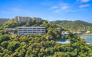 Um hotel de vários andares com piscina numa encosta, rodeado por vegetação exuberante e com vista para a costa.