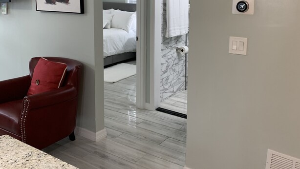 A modern hotel room with a granite countertop, a red leather chair, a painting of a panda, a bed with white linens, and a bathroom with a marble shower.