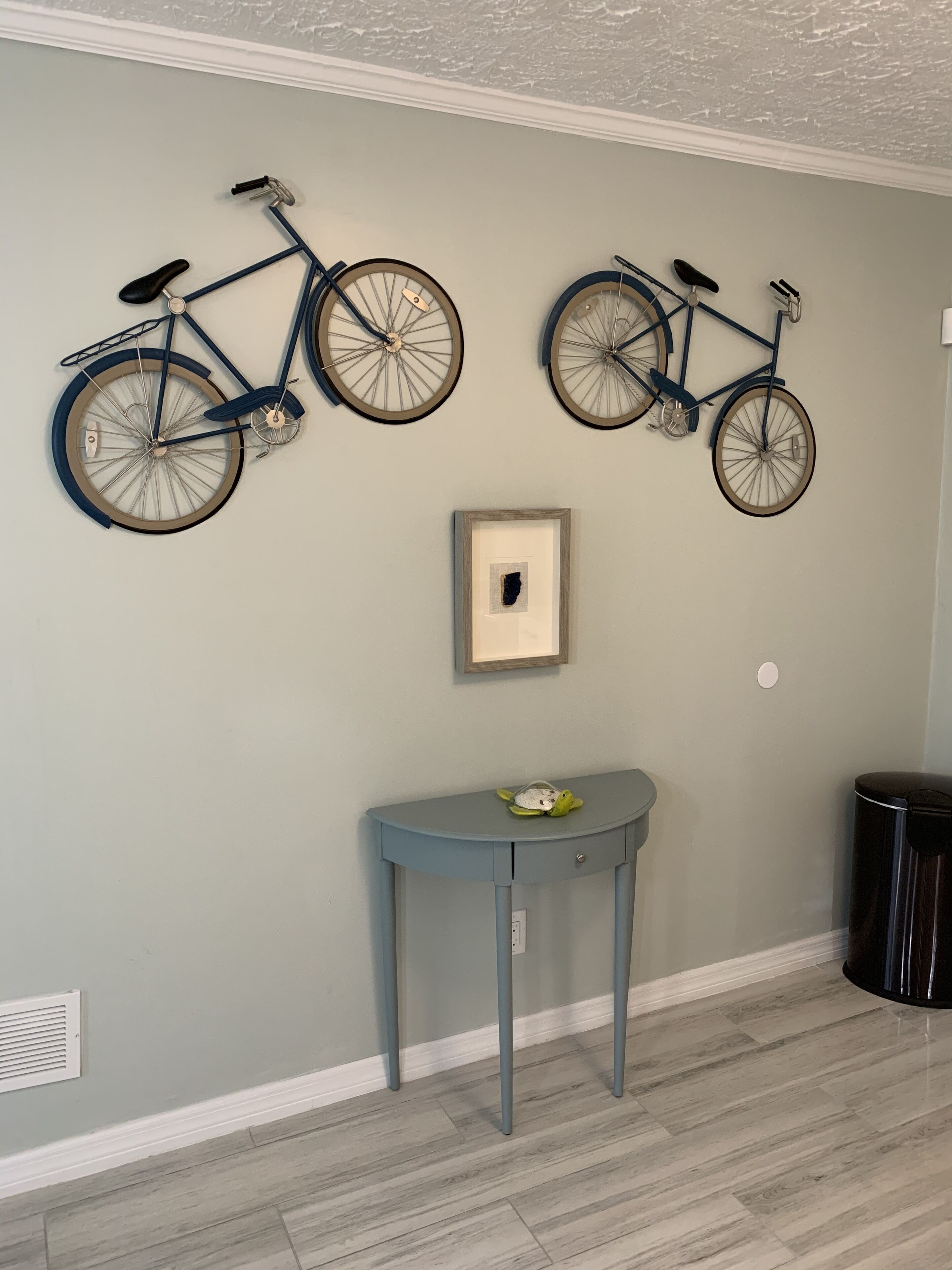 A room with two wall-mounted bicycles, a small table with a turtle figurine, and a trash can.