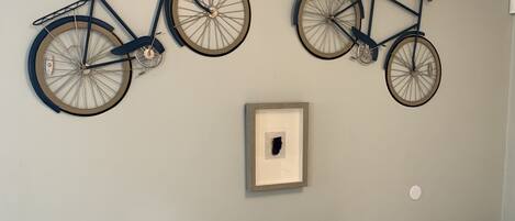 A room with two wall-mounted bicycles, a small table with a turtle figurine, and a trash can.