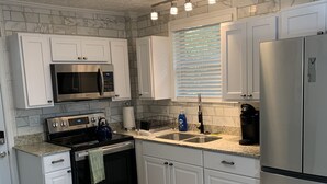 A modern kitchen with white cabinetry, stainless steel appliances, a granite countertop, and a wooden floor.