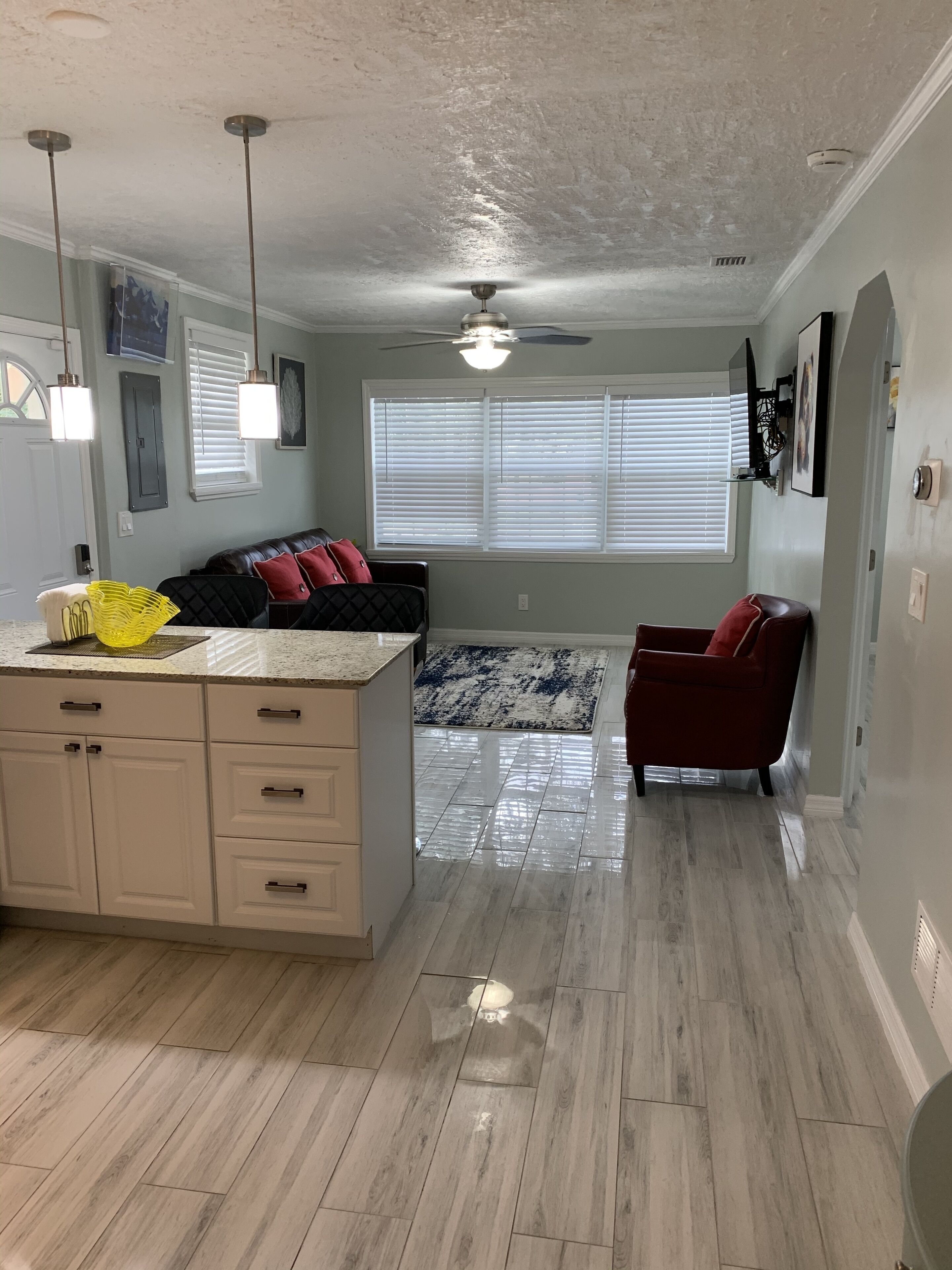 A spacious living area with a kitchen, a ceiling fan, and a large window with blinds.