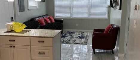 A spacious living area with a kitchen, a ceiling fan, and a large window with blinds.