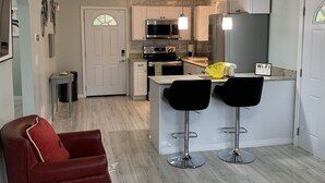 A modern kitchen with white cabinets, a black countertop, and a bar area with two stools.