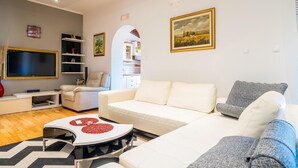 Una sala moderna con un sofá blanco, una mesa de centro con pétalos de flores rojas, un televisor y un cuadro de un campo.