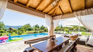 Un patio exterior con piscina, mobiliario de madera y vistas al paisaje.