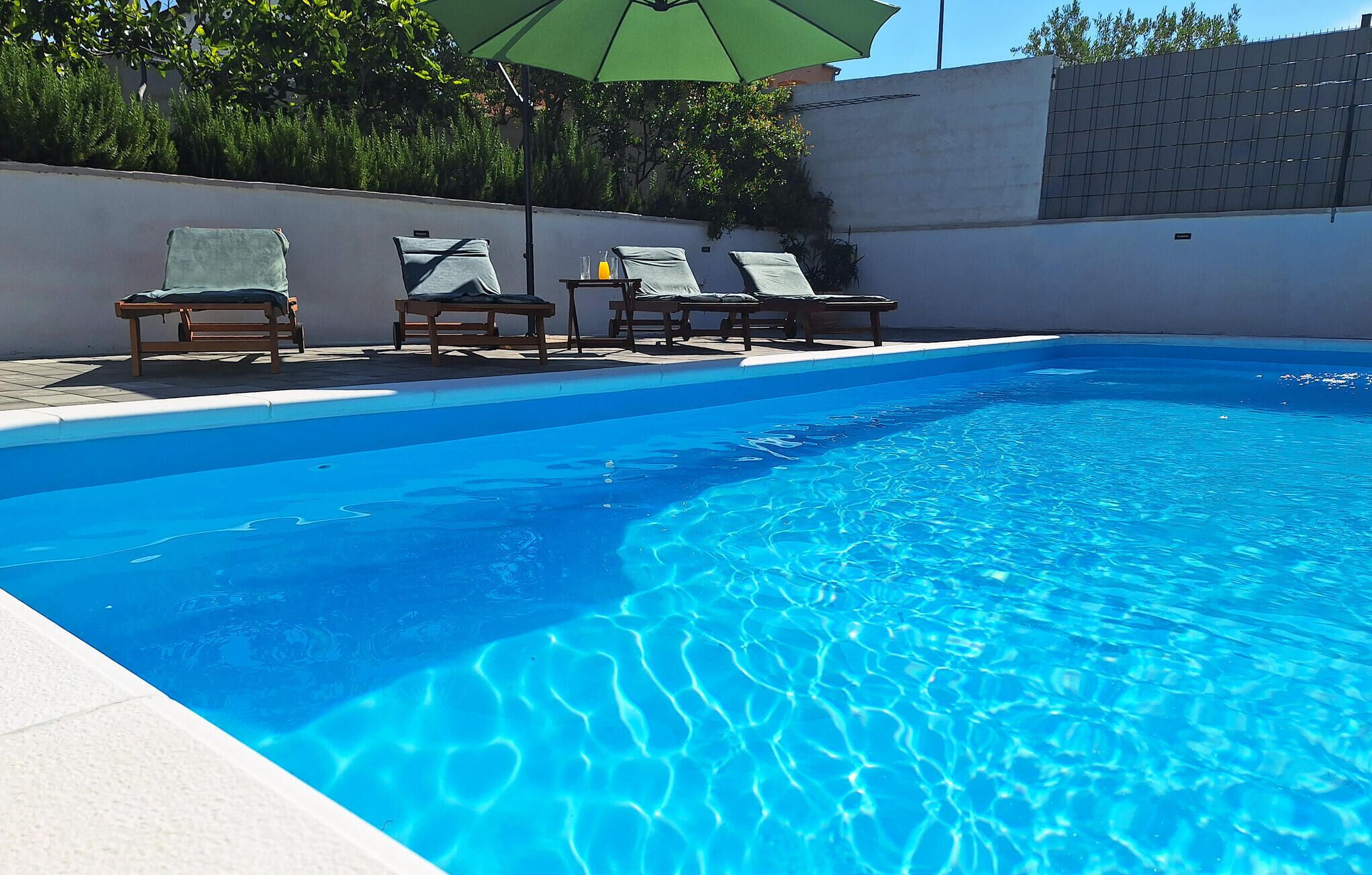 A clear blue swimming pool with lounge chairs and a table with drinks.